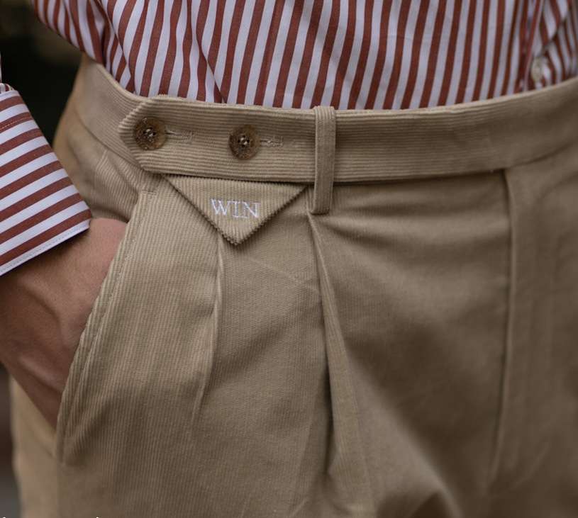 Beige Cordhose mit Bundfalten, geknöpfter Lasche am hohen Bund und gesticktem Monogramm, rot gestreiftes Hemd