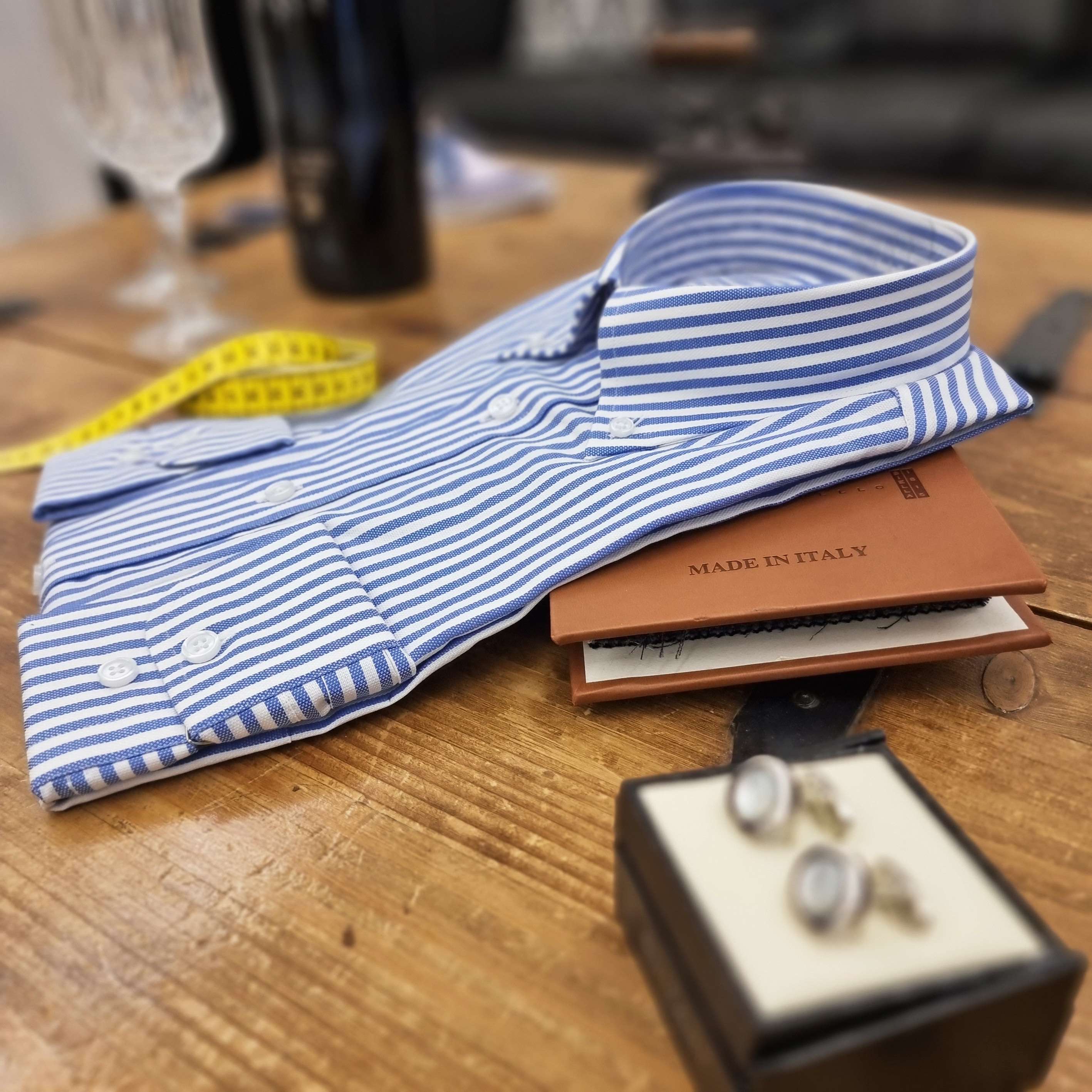 Blau-weiss gestreiftes Masshemd mit Etikett Made in Italy, Massband und Manschettenknöpfen auf einem Holztisch